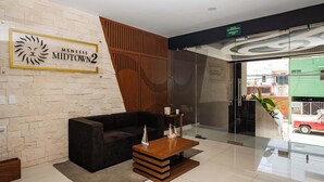 A reception area with a stone wall, a wooden panel design, a black sofa, and a wooden coffee table with model ships. - Charming Stay – 5 Minutes from Walmart & 5th Avenue (Playa del Carmen)