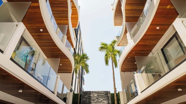 A modern building with a central atrium, wooden ceiling, and glass balconies. - Charming Stay – 5 Minutes from Walmart & 5th Avenue (Playa del Carmen)