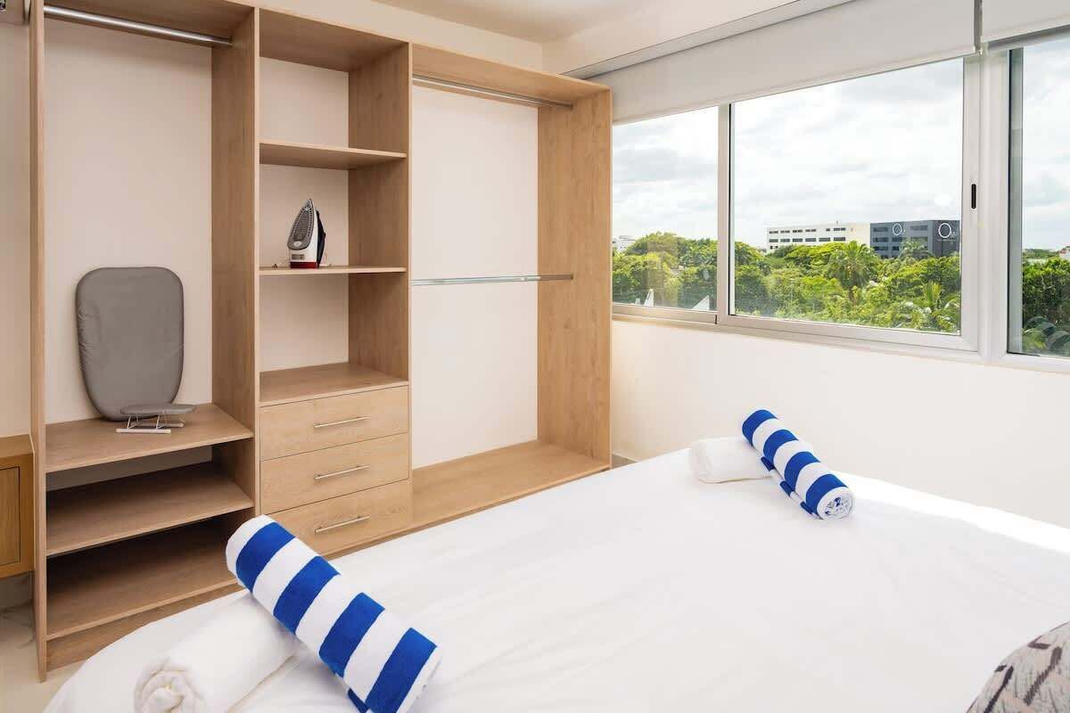 Ein modernes Schlafzimmer mit einem großen Bett, einem Kleiderschrank mit vielen Fächern, einem Sessel und Blick ins Grüne.