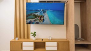 A flat-screen TV mounted on a wall above a wooden console with drawers, a small potted plant, and a decorative item. - Warmth and Charm in Harmony (Cancún)