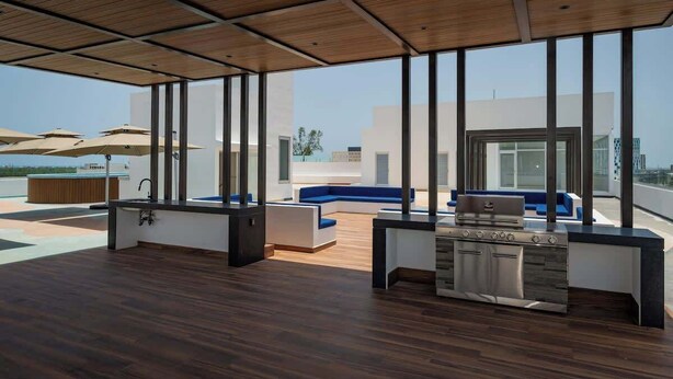 A modern outdoor kitchen area with a built-in grill, seating, and large windows offering a city view. - Warmth and Charm in Harmony (Cancún)
