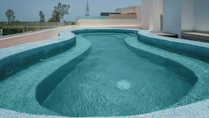 A modern swimming pool with a curved design, surrounded by a low wall and a clear view of the city skyline in the background. - Warmth and Charm in Harmony (Cancún)