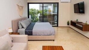 Un soggiorno moderno con divano, letto, tavolino con mele, televisore e balcone con piante.