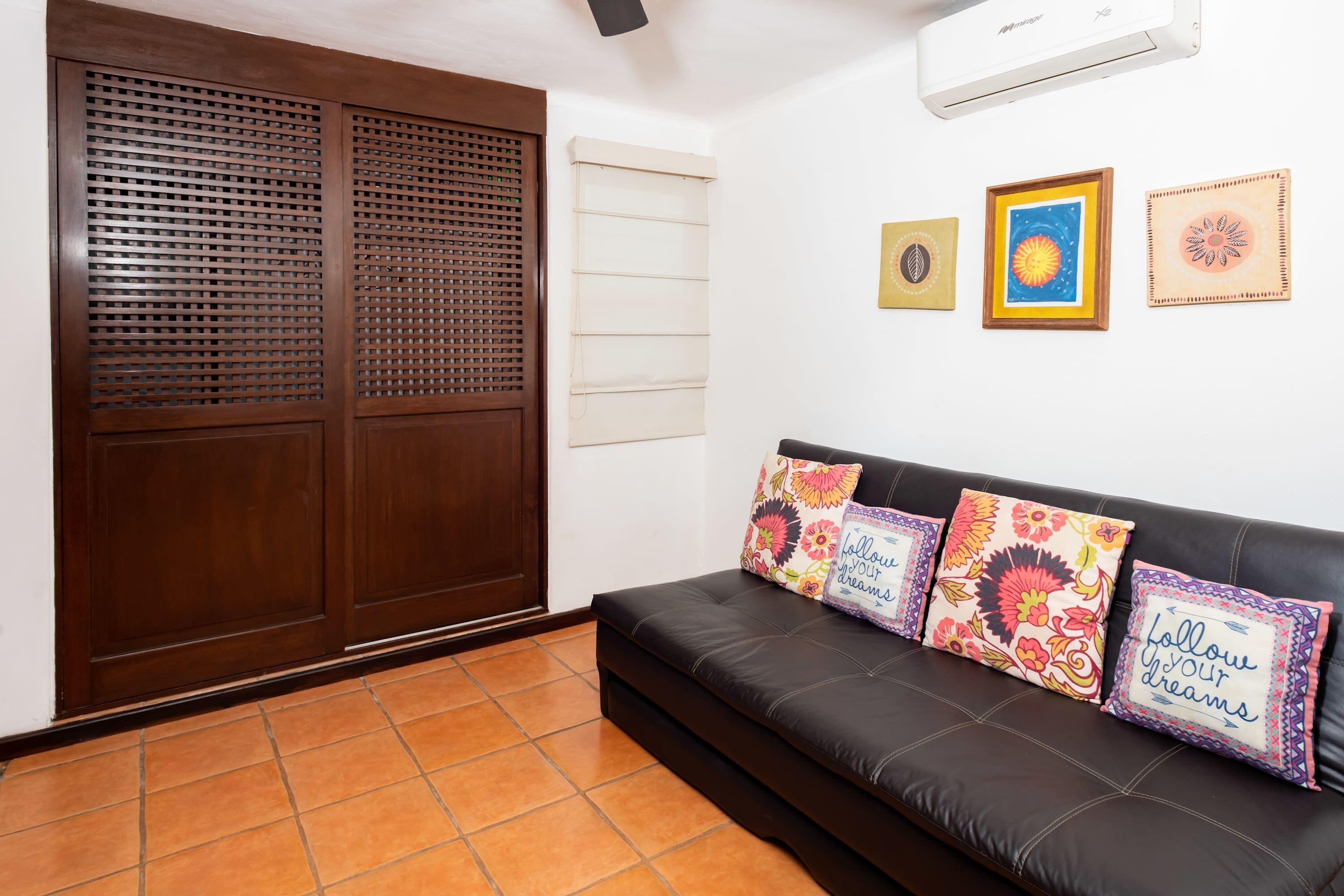 A room with a black leather sofa, wooden wardrobe, and three framed artworks on the wall.