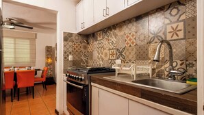 Cocina con estufa, lavamanos y salpicadero con diseño. Hay un comedor con sillas anaranjadas y una mesa.