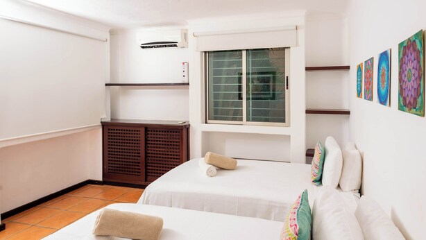 Habitación de hotel con dos camas, una ventana con persianas, un armario pequeño y decoración en la pared.