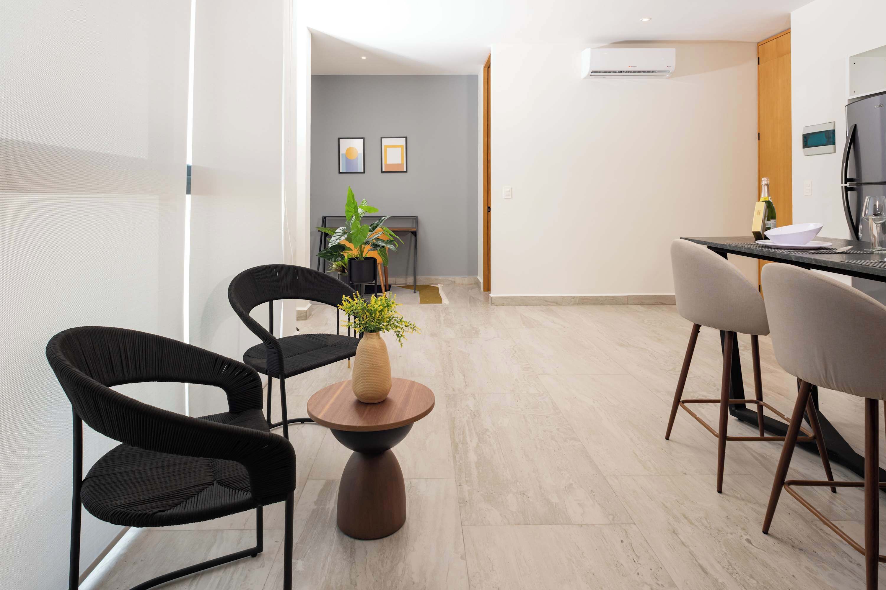 A modern hotel room with a dining area featuring black chairs, a round wooden table, and a potted plant.