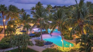 A resort pool area with palm trees, lounge chairs, and a view of the ocean. - Studio Double@ Elysian Beach Resort (St Thomas)