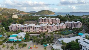 A resort with multiple buildings, a beach area with palm trees, and a view of the sea and hills in the background. - Studio Double@ Elysian Beach Resort (St Thomas)