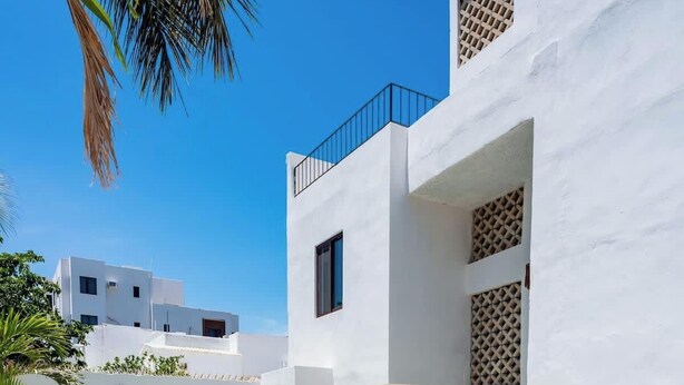 A modern white building with a pool, surrounded by potted plants and palm trees. - Strategically located suite with desk (Cancún)