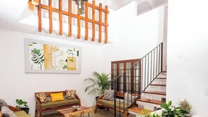A living room with a wooden staircase, a sofa with cushions, a coffee table, and a large abstract painting on the wall. - Strategically located suite with desk (Cancún)