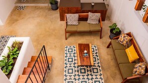 Un amplio salón con escalera de madera, ventilador de techo y alfombra estampada.