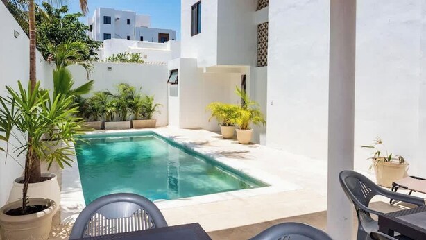 Un área de piscina con plantas en macetas y una mesa con sillas.
