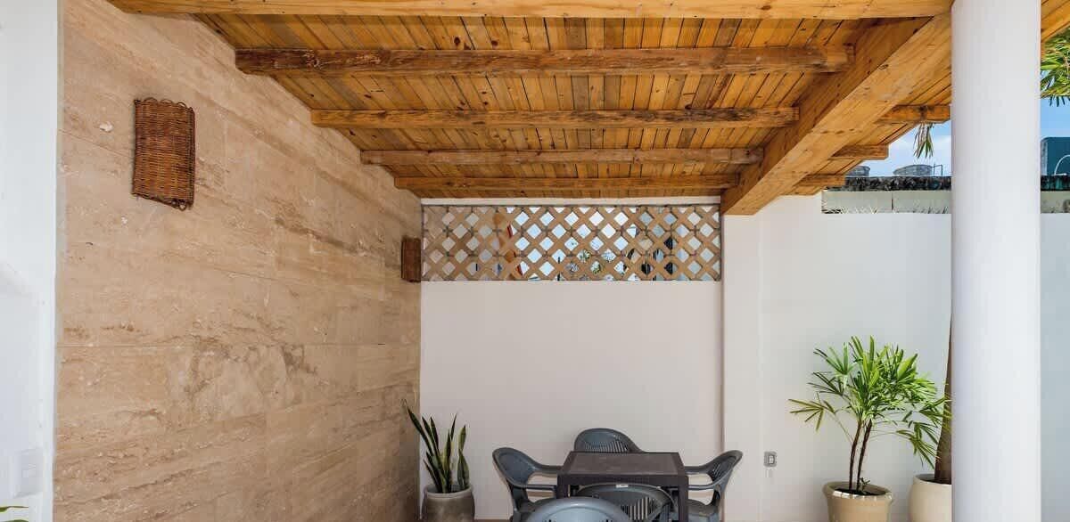 A covered patio with a wooden ceiling, a lattice partition, and a table with chairs.