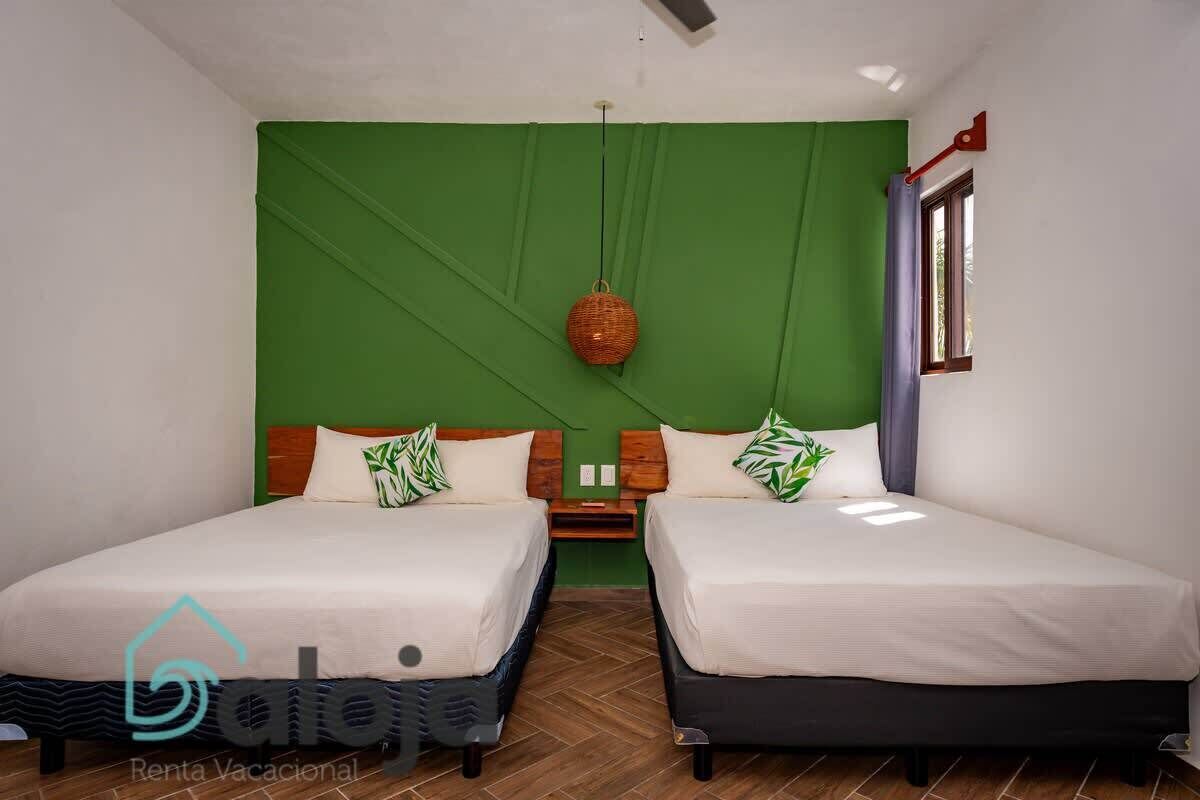 Una habitación con dos camas, una pared verde decorativa, una cesta colgante y una ventana con cortinas.