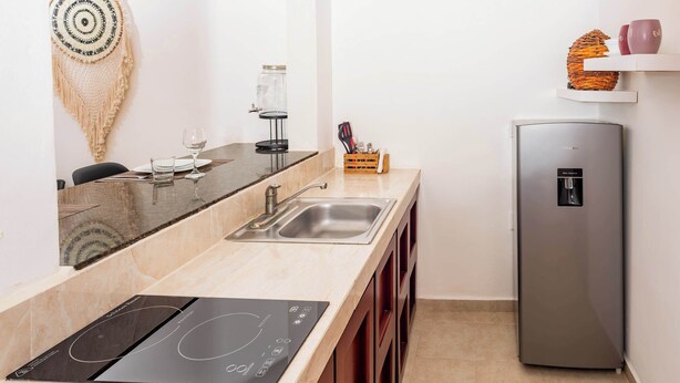A modern kitchen with a built-in induction cooktop, a stainless steel refrigerator, and a small sink. - Cozy Xiu Suite in Arenika (Puerto Morelos)