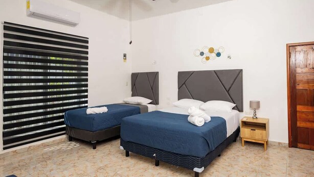 A hotel room with two beds, a wooden door, a small bedside table, and a wall-mounted air conditioner. - Villa for groups in excellent location (Playa del Carmen)