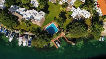 An aerial view of a resort with a swimming pool, boats, and villas.