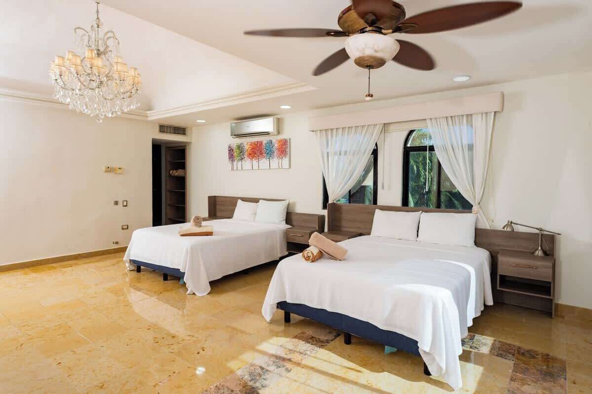 Une chambre d’hôtel avec deux lits, un lustre, un ventilateur de plafond et une grande fenêtre avec des rideaux.