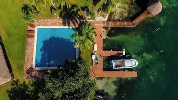 An aerial view of a resort with a swimming pool, a wooden deck, and a boat dock.