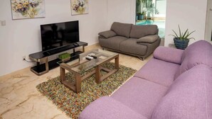 A living room with a flat-screen TV, a gray sofa, a purple sofa, and a glass coffee table. - Magnificent 2 blocks from the beach and 5th Ave. (Playa del Carmen)