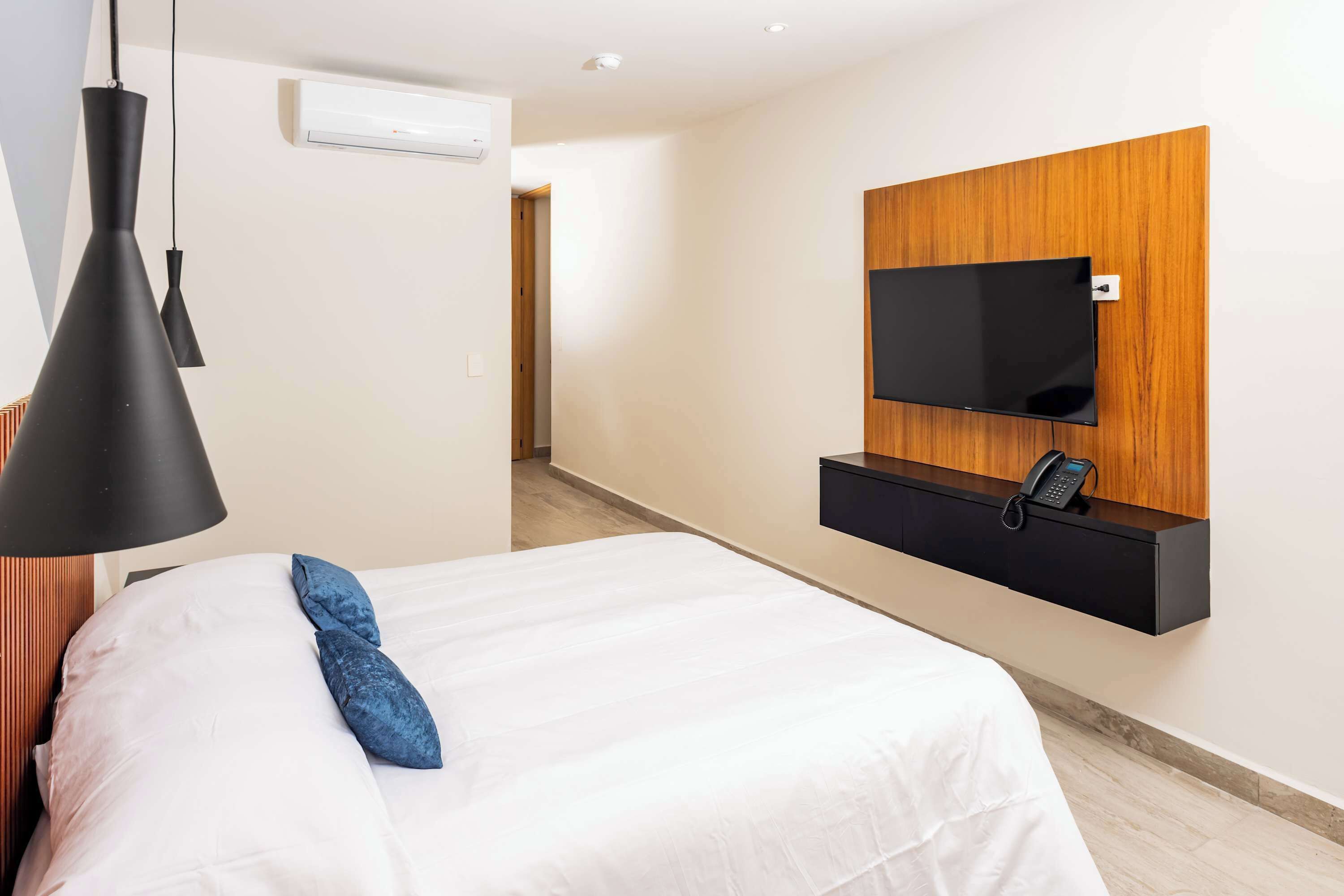 A hotel room with a bed, a TV mounted on a wooden panel, and a telephone on the panel.