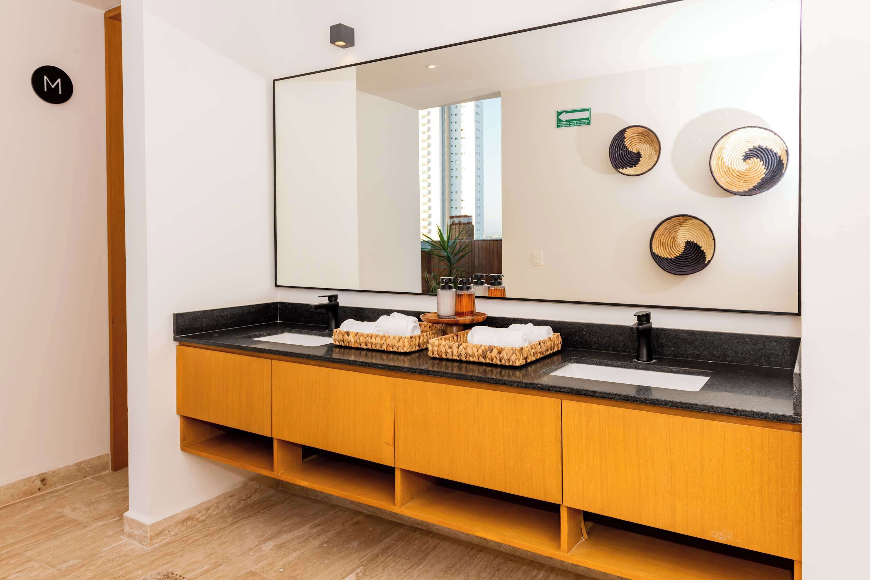 A modern bathroom with a large mirror, two sinks, and a wooden vanity.