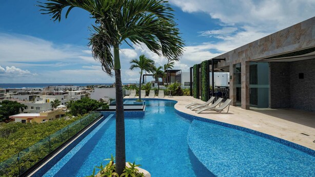 A modern infinity pool with a view of the ocean, surrounded by palm trees and lounge chairs. - Playa del Carmen Apartment: Rooftop Pool, City Views (Playa del Carmen)