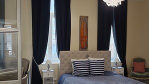 Une chambre à coucher avec un grand lit, deux tables de chevet, un lustre et une fenêtre avec des rideaux.