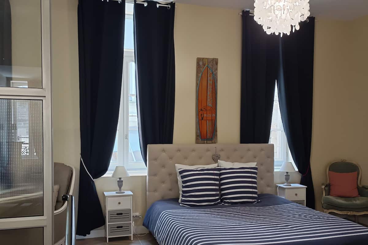 Een slaapkamer met een groot bed, twee nachtkastjes, een kroonluchter en een raam met gordijnen.