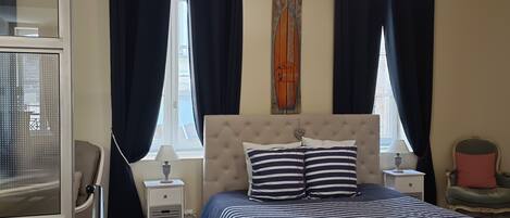 Ein Schlafzimmer mit einem großen Bett, zwei Nachttischen, einer Chandelierleuchtre und einem Fenster mit Vorhängen.