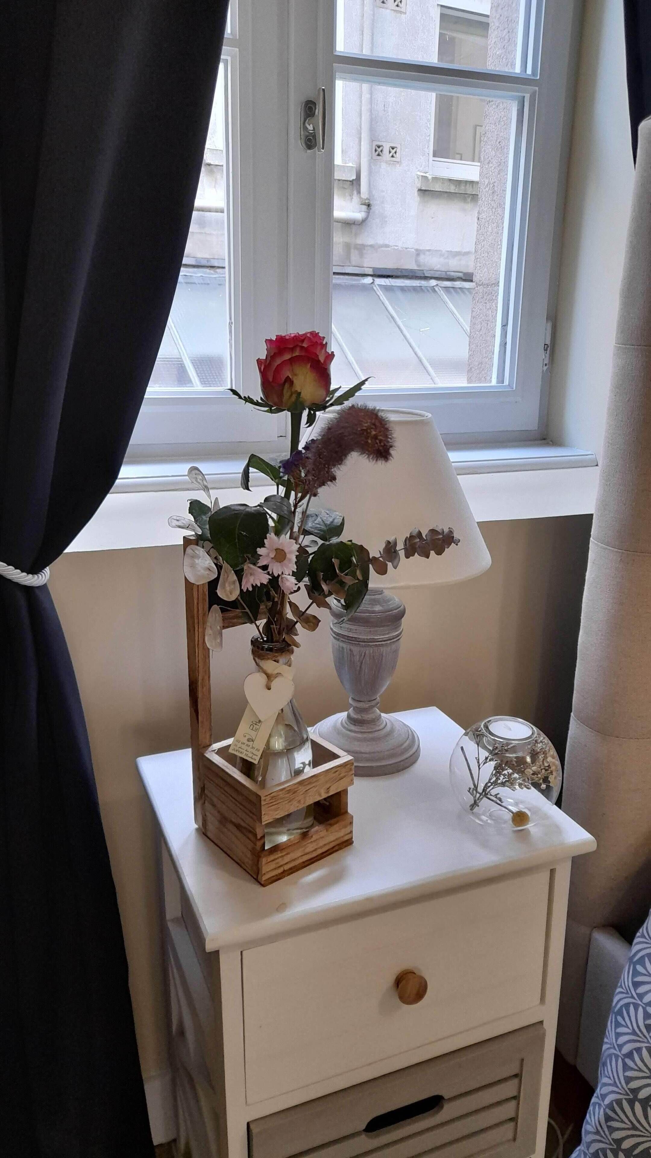 Ein Nachttisch mit Blumen in einer Vase, einer Lampe und einer kleinen Holzschatulle.