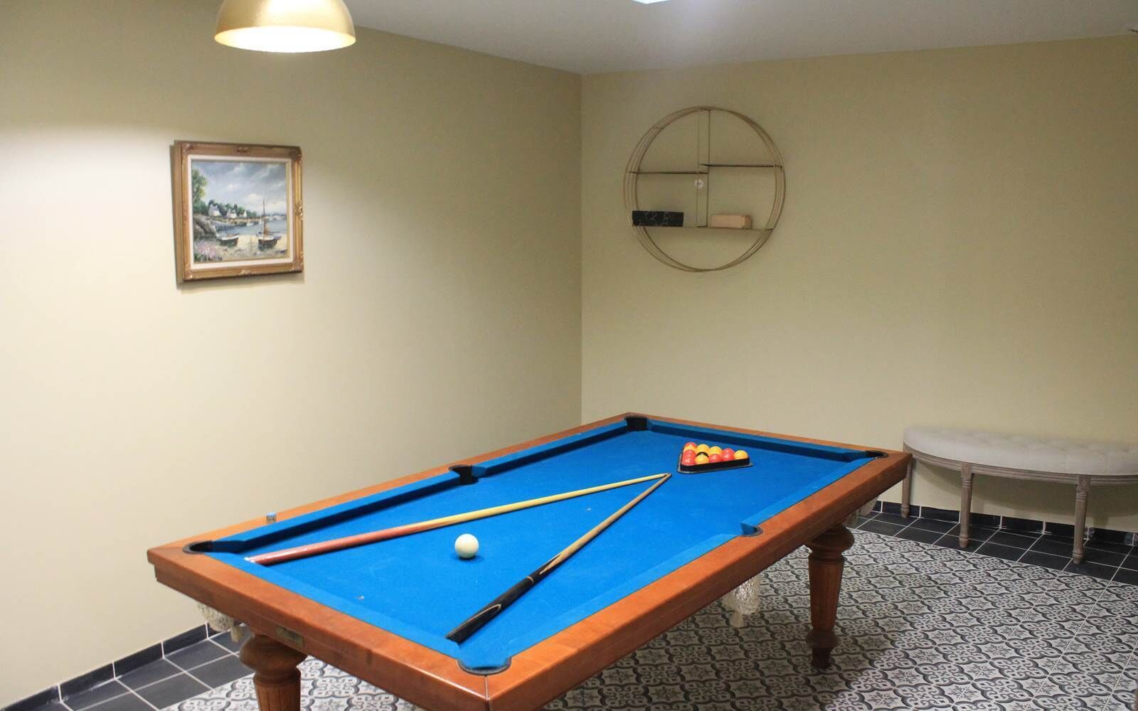 Una mesa de billar con superficie azul de fieltro, una vara y un juego de bolas de billar.