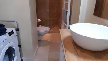 A compact bathroom with a washing machine, toilet, and a large sink.