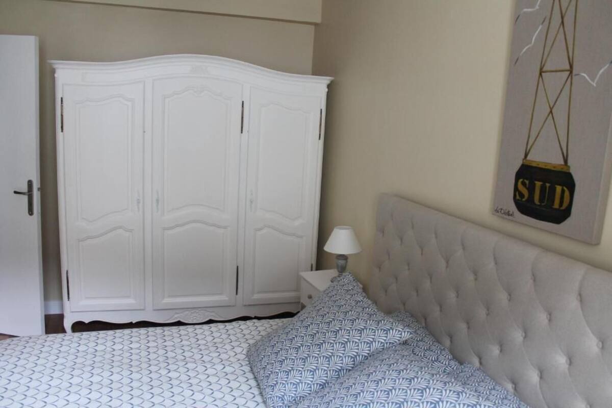 Een slaapkamer met een bed, een witte kledingkast, een nachtkastje en een kunstwerk aan de muur.