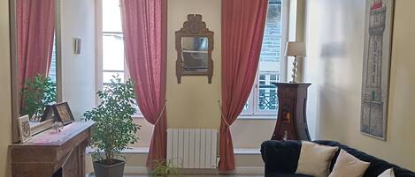 A living room with a chandelier, red curtains, a black sofa, a small table, and a potted plant.