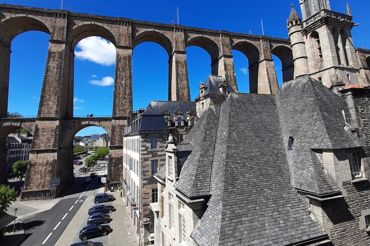 Een historische stenen brug met meerdere bogen, een kerk met een torenspits, en een straat met geparkeerde auto's.