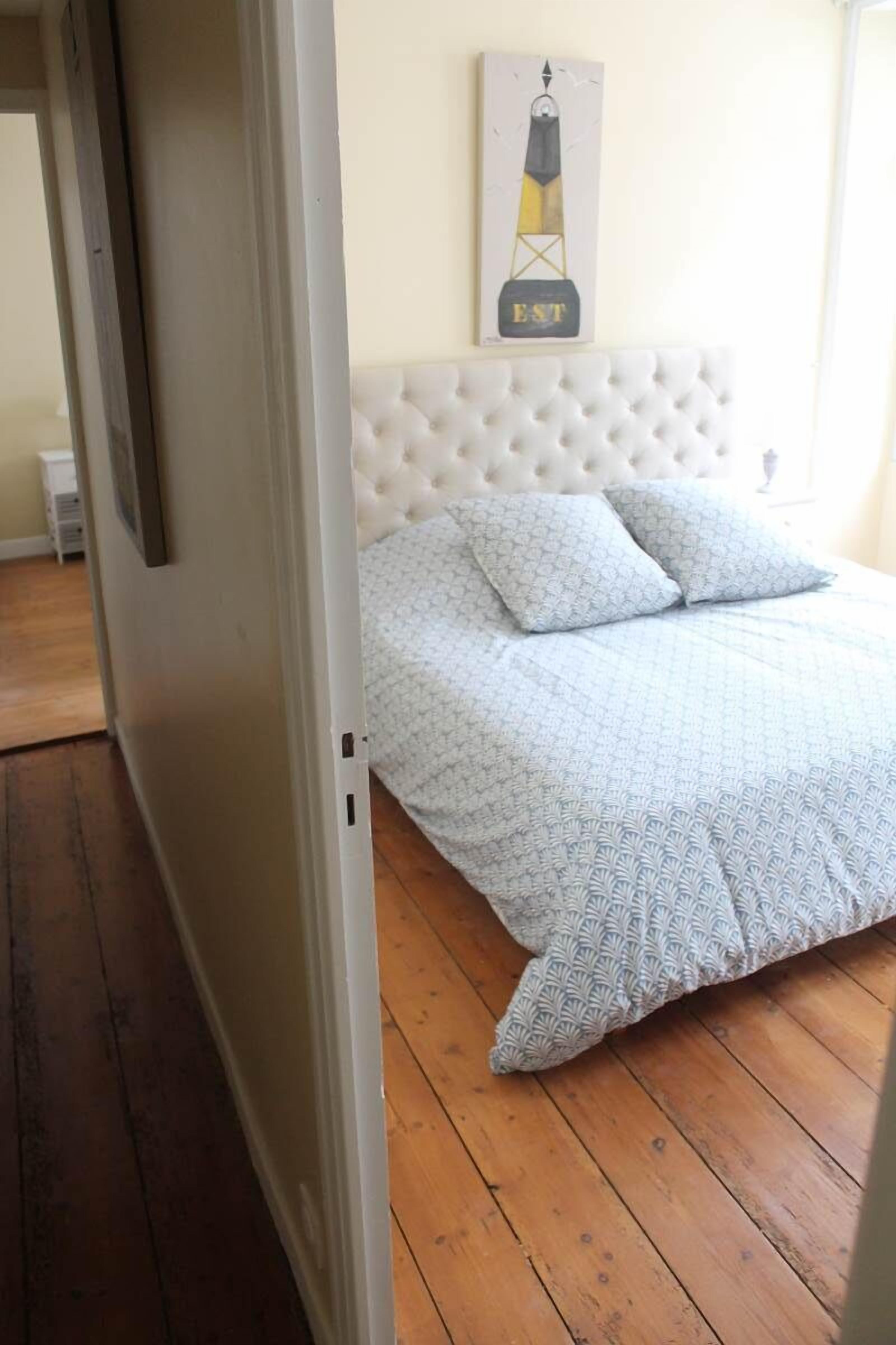 A bedroom with a tufted headboard, a bed with patterned bedding, and a painting on the wall.