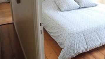 Un dormitorio con cabecera capitonada, cama con ropa de cama estampada y un cuadro en la pared.