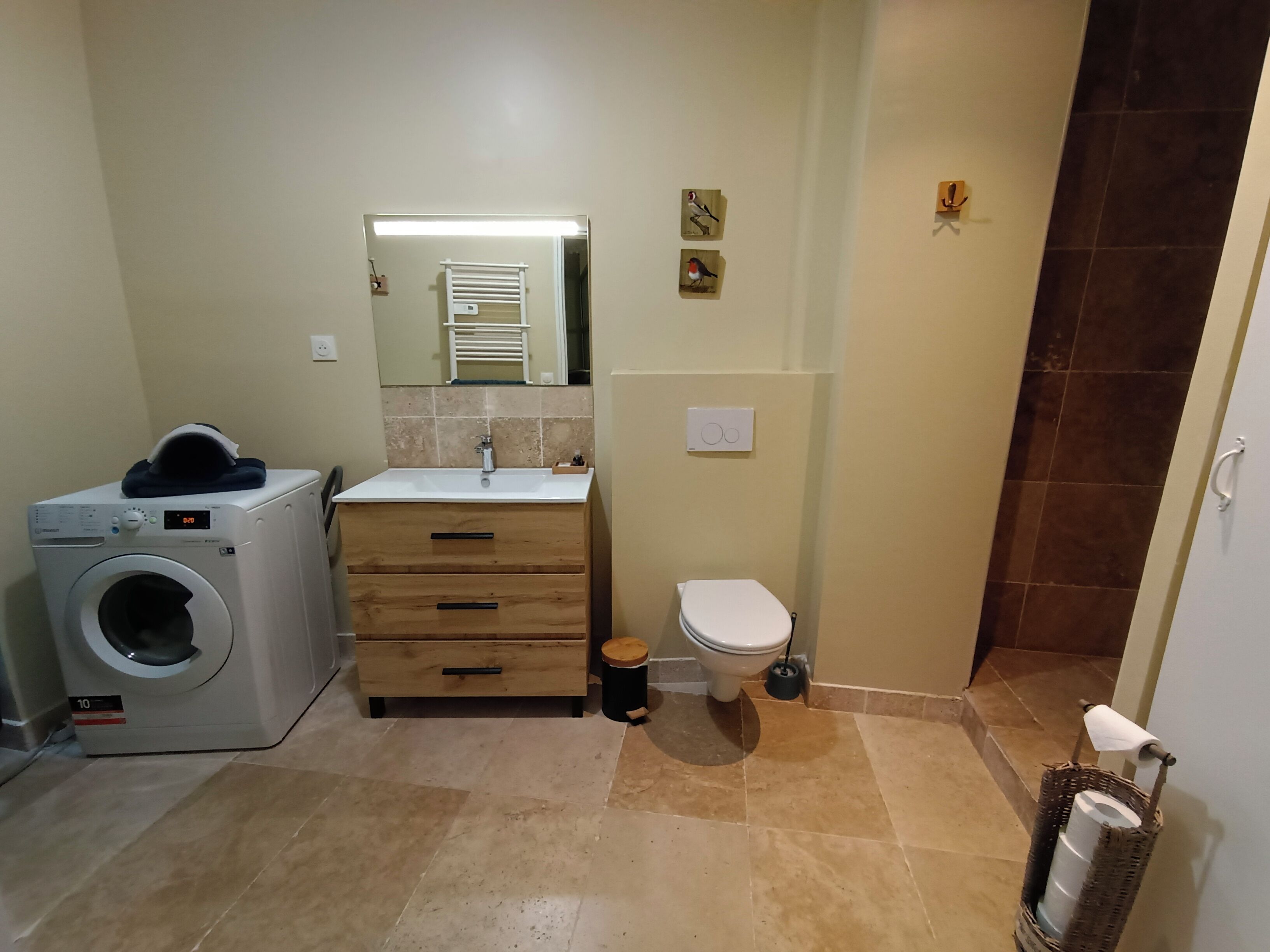 A compact bathroom with a washing machine, a sink, a toilet, and a small mirror.