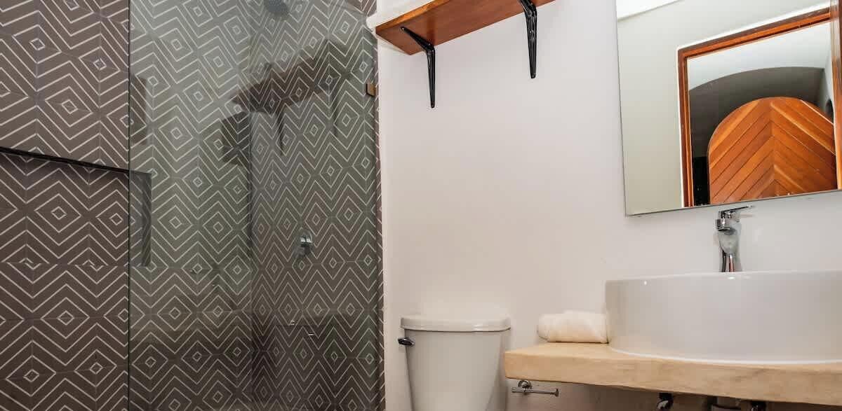 A bathroom with a toilet, a sink, a mirror, and a shower.
