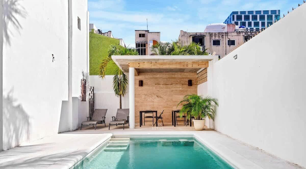 A pool area with a wooden pergola, lounge chairs, and potted plants.