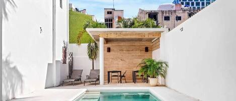 A pool area with a wooden pergola, lounge chairs, and potted plants.