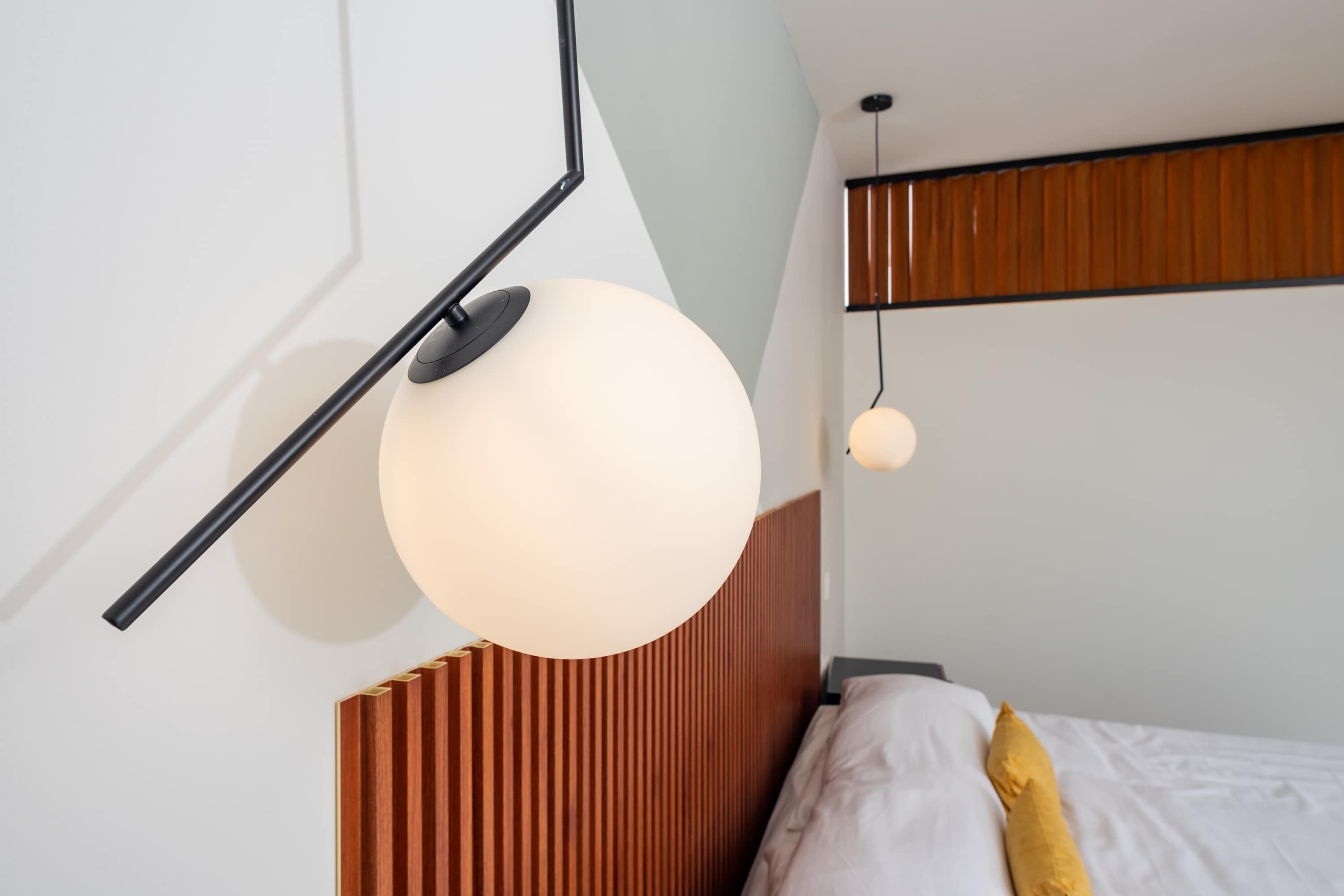 A modern bedroom with a slanted ceiling, a wooden headboard, and a hanging spherical light fixture.