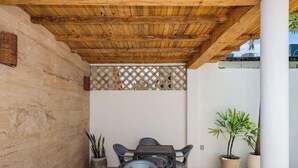 Een overdekt terras met houten balken, een tafel met stoelen en potplanten.