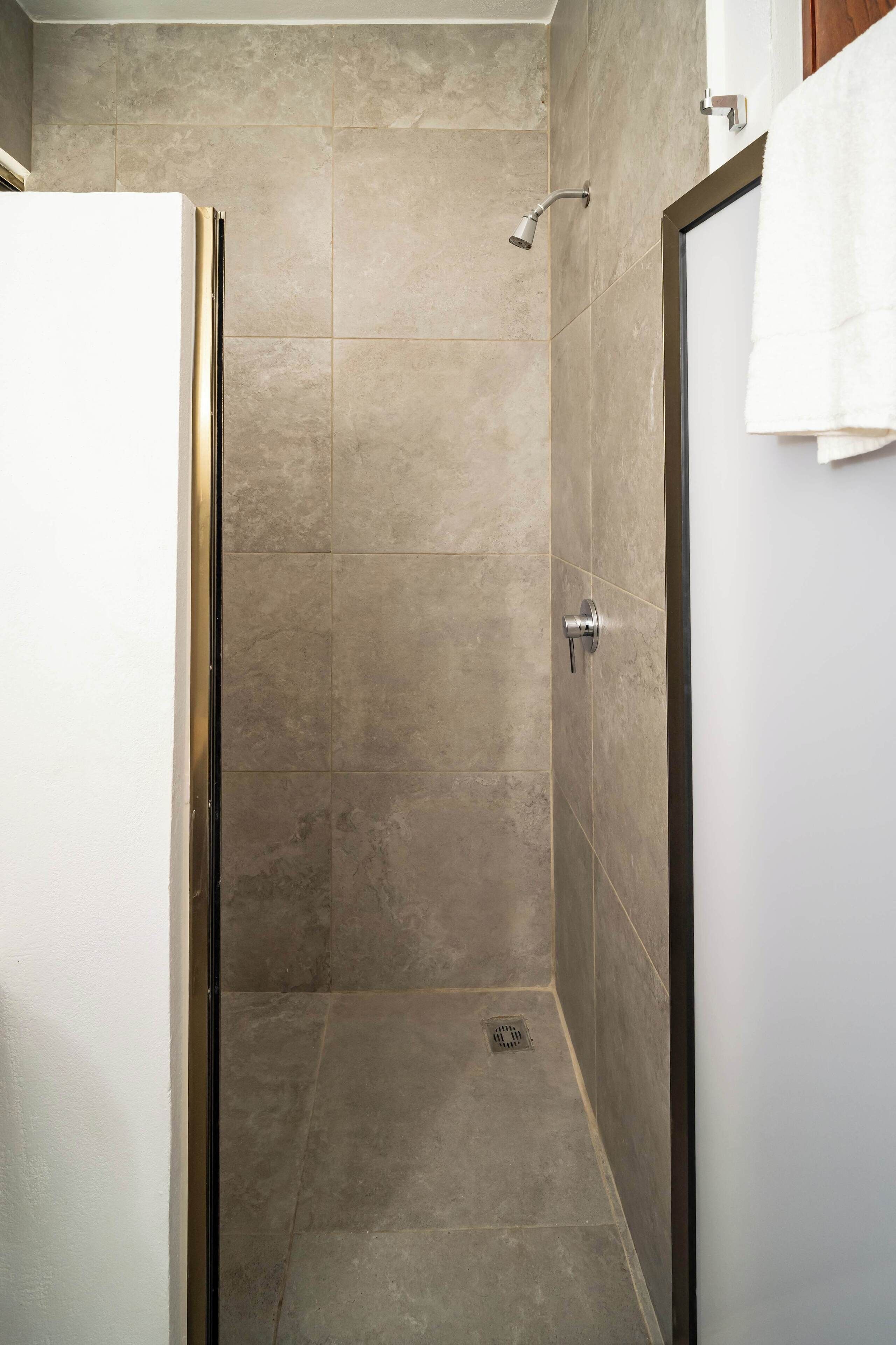 A bathroom with a shower, tiled walls, a white door, and a towel hanging on the wall.