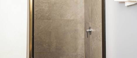 A bathroom with a shower, tiled walls, a white door, and a towel hanging on the wall.
