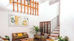 Una sala de estar con una escalera de madera, un sofá con cojines, una mesa de centro y un cuadro abstracto grande en la pared.