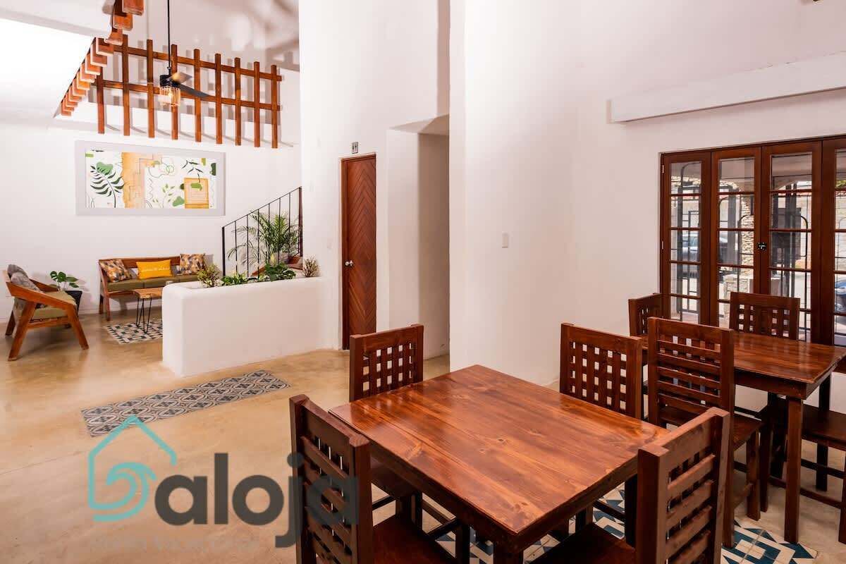 Uma sala de estar ampla com uma mesa de jantar de madeira e cadeiras, um sofá, uma escada e uma janela grande.