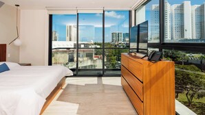 A modern bedroom with a large bed, a wooden dresser, and a city view through floor-to-ceiling windows. - Charm and modernity together (Cancún)